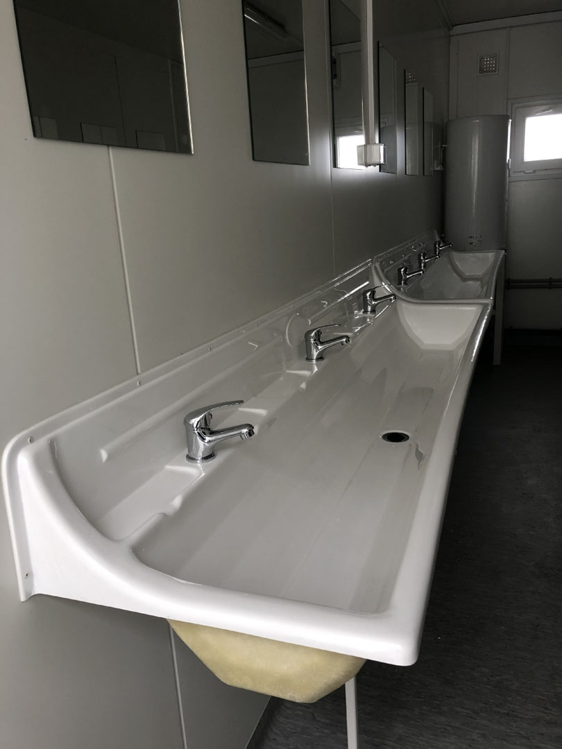 Elementy sanitarne-galeria volmar (10) Wyposażenie sanitarno-higieniczne z długą umywalką i lustrami w jasnym pomieszczeniu.